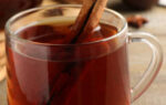 Glass cup of hot tea with aromatic cinnamon on wooden table. Space for text